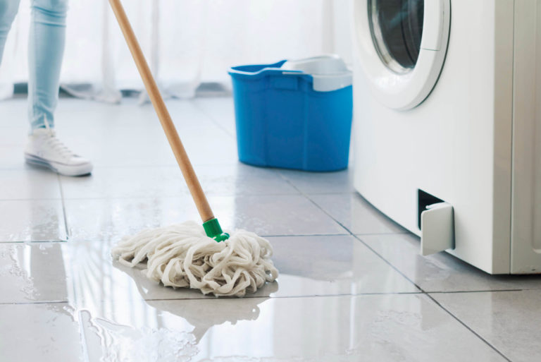 Woman mopping up water leak on tile floor beside washing machine.