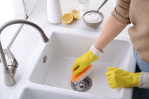 Person cleaning sink to prevent kitchen drain clogs